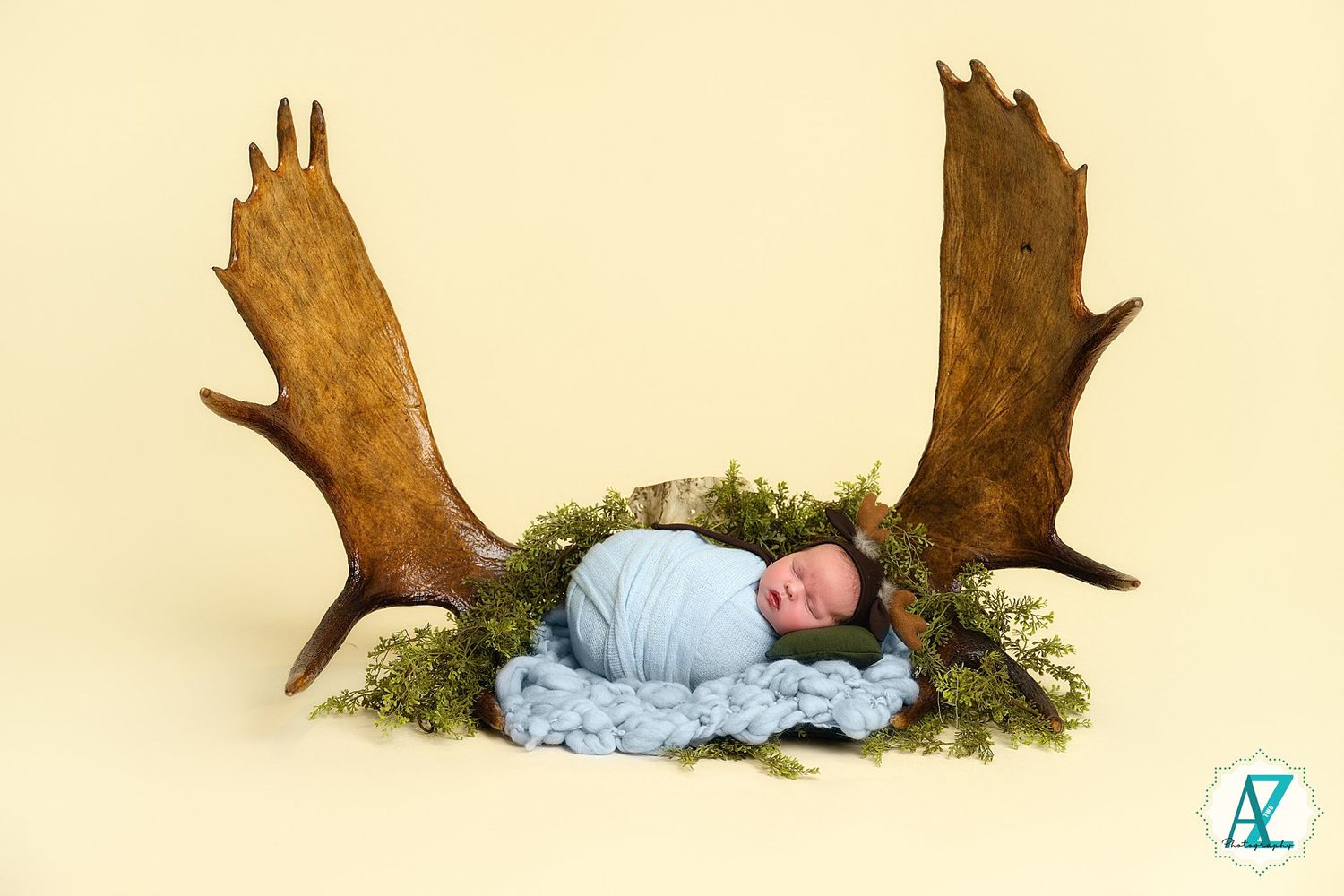 Baby in light blue outfit posed next to rustic wood elements in studio setting.