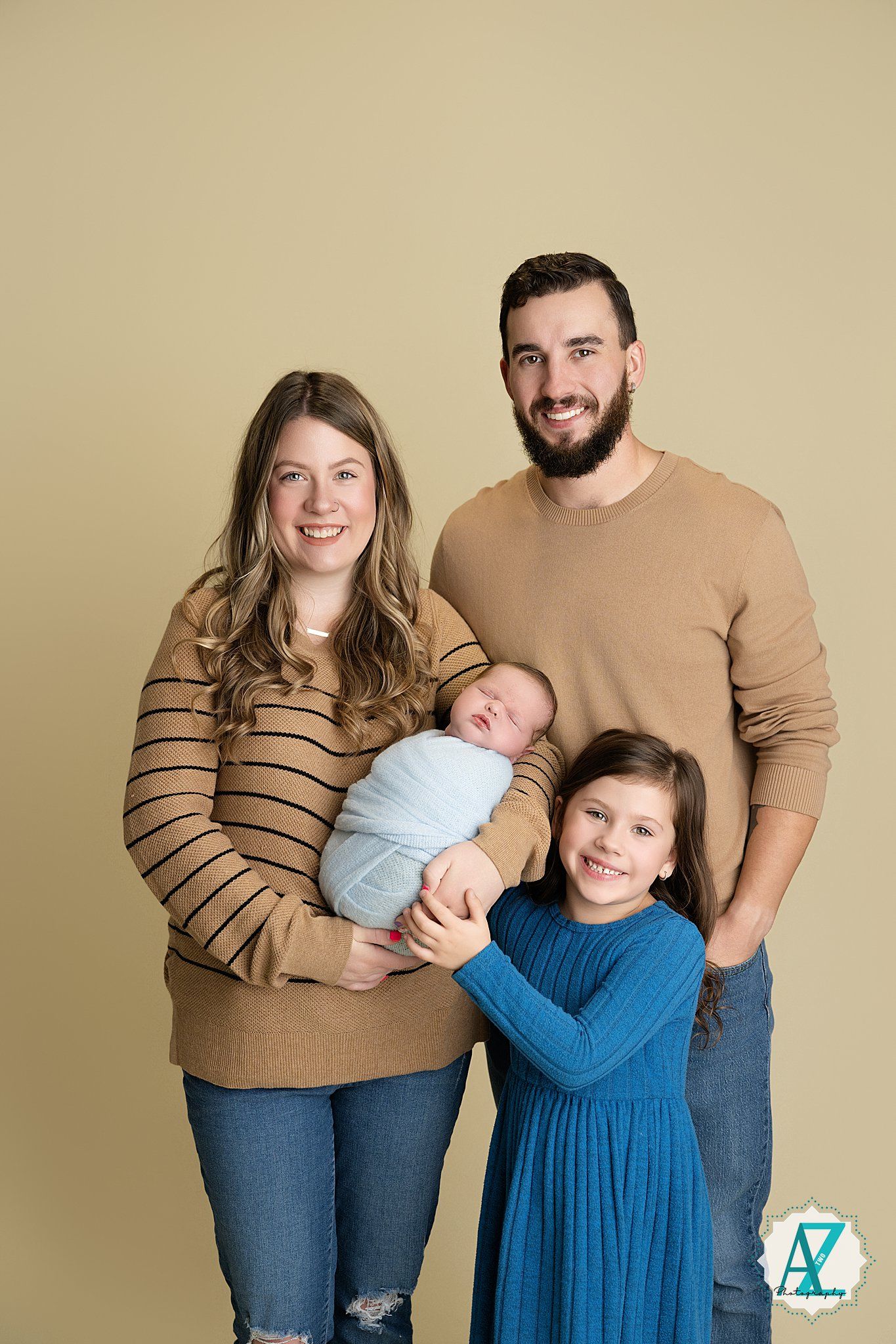 Family wearing coordinated outfits in tan and blue share intimate moments during a studio photoshoot.