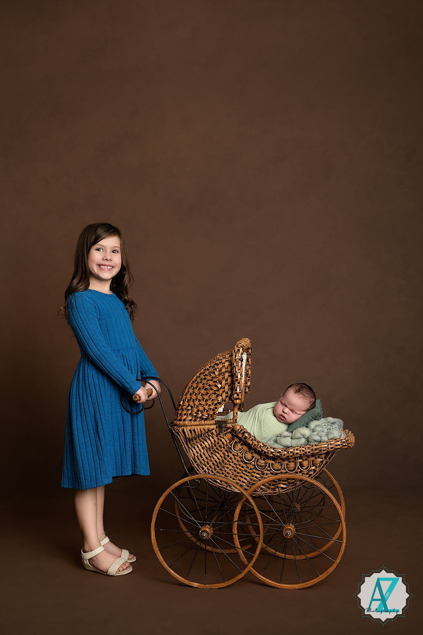 Side view of vintage wicker pram with blue-dressed figure and brown studio background.