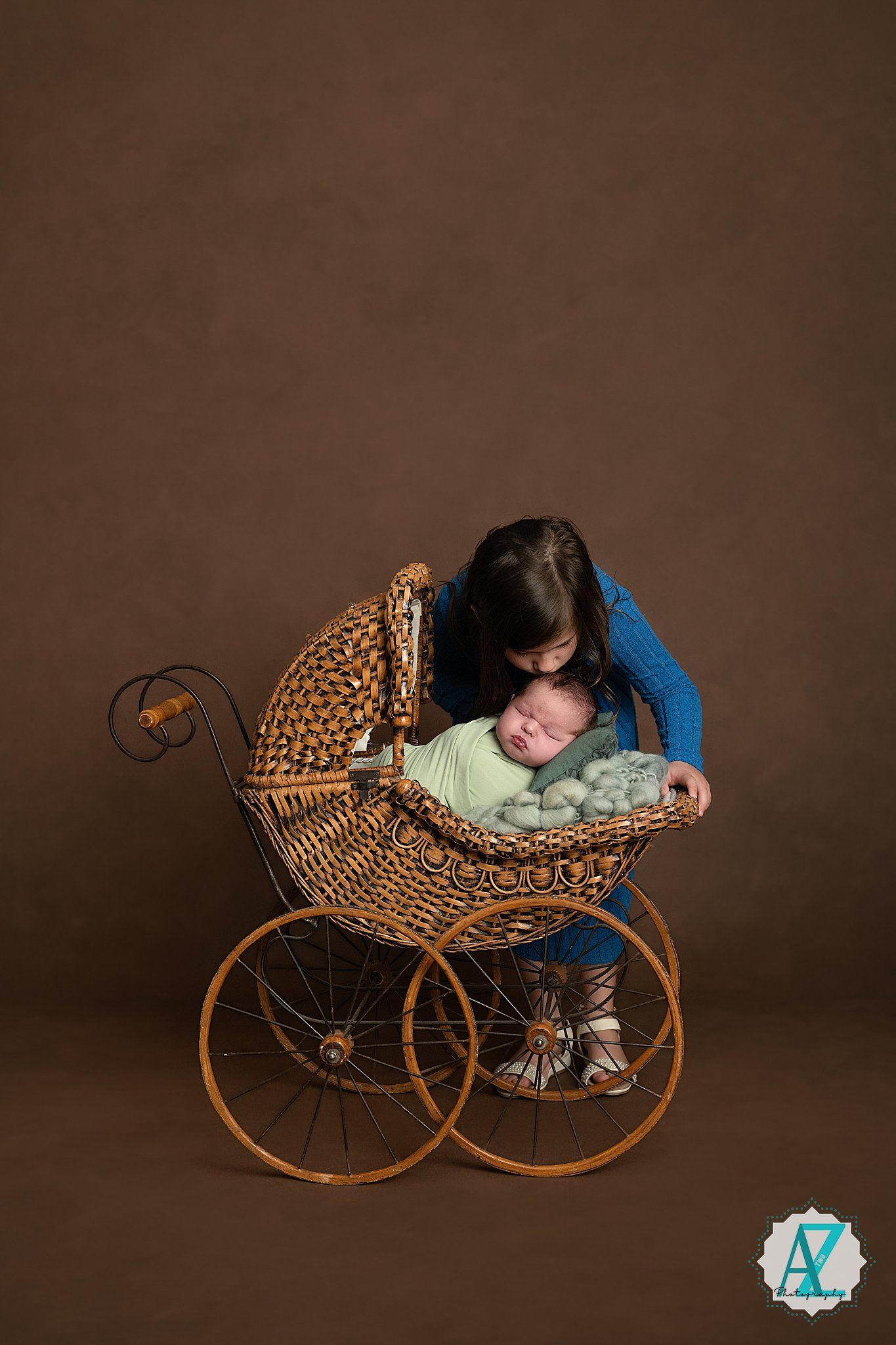 Baby sleeping peacefully in an antique wicker pram against a brown studio background.