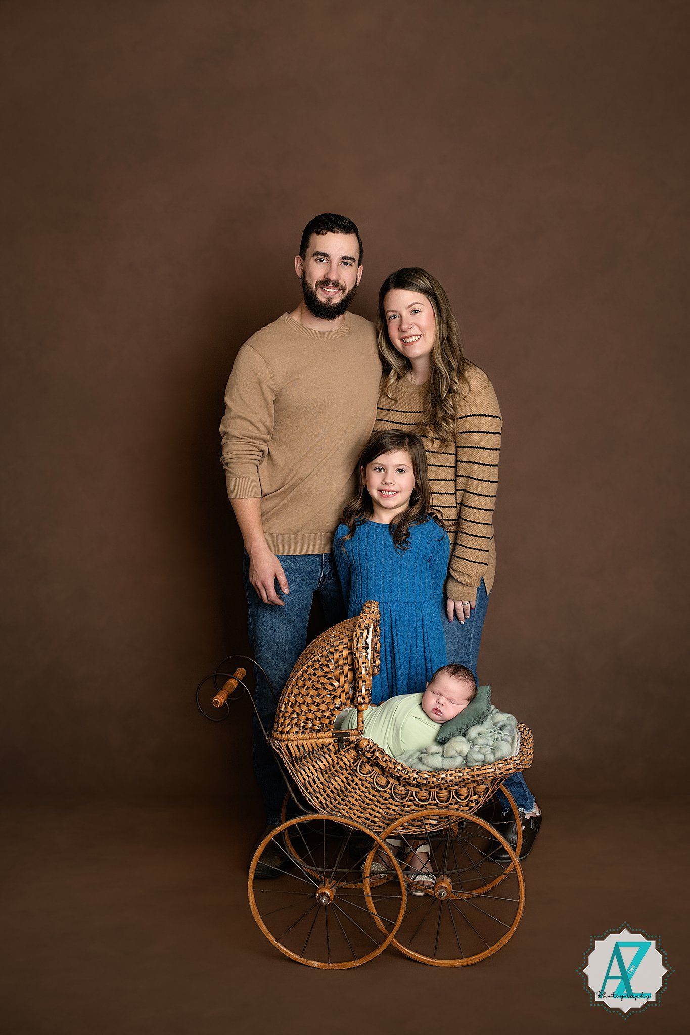 A vintage wicker baby carriage with family portrait setup against a dark brown studio backdrop.