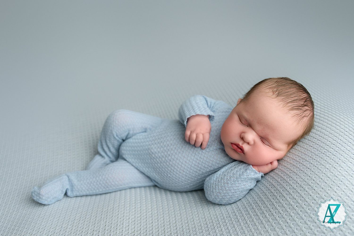 Peaceful sleeping newborn baby wearing soft blue knit outfit on textured gray background.
