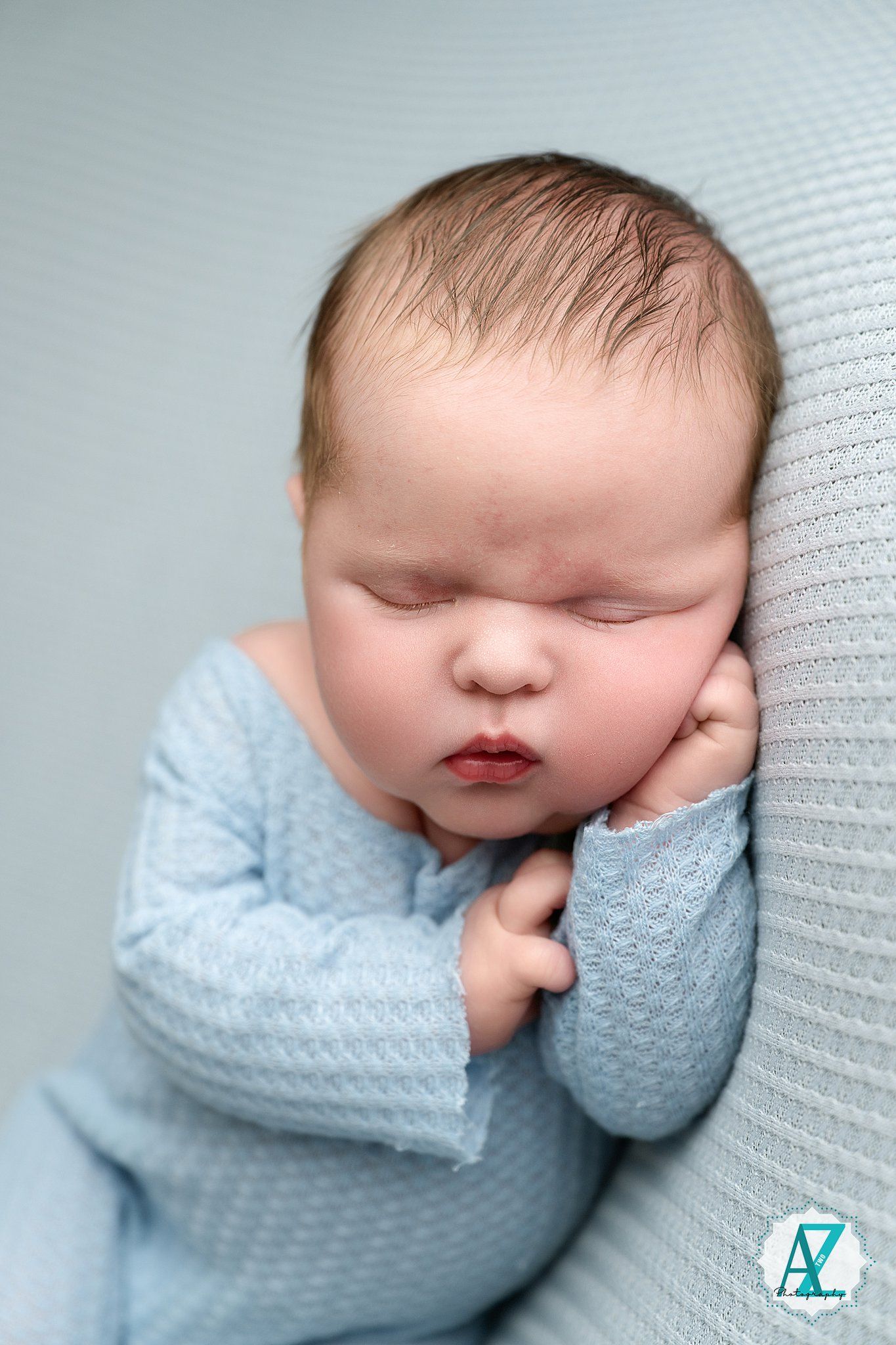 Sleeping baby wearing soft blue knit clothing lies peacefully against textured white bedding.