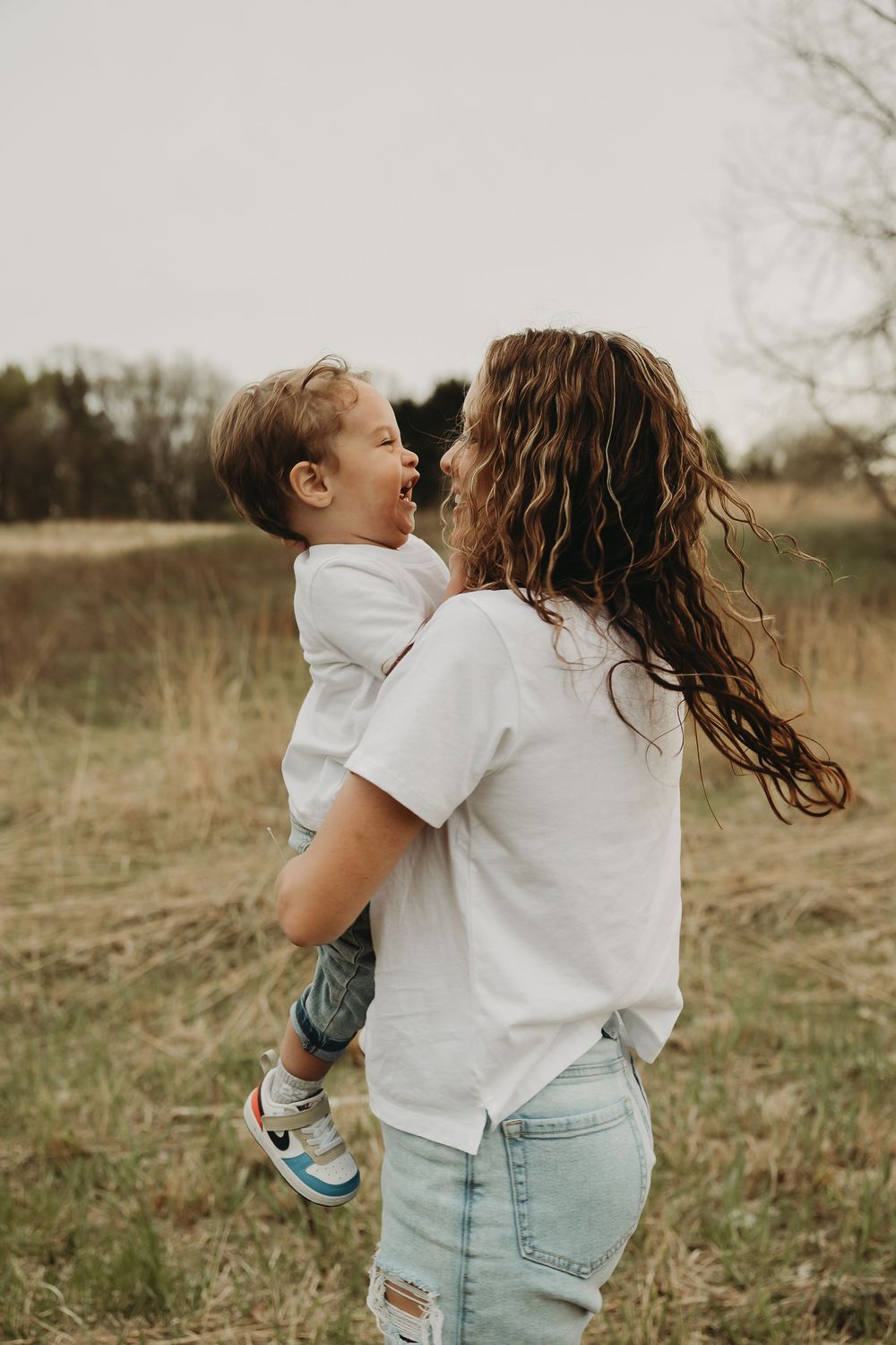 A candid outdoor moment between parent and child playing together in a grassy field during golden hour.
