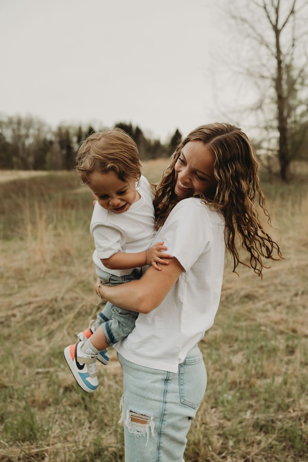 A joyful candid moment captured outdoors in a field with matching white shirts and light denim on an overcast day.