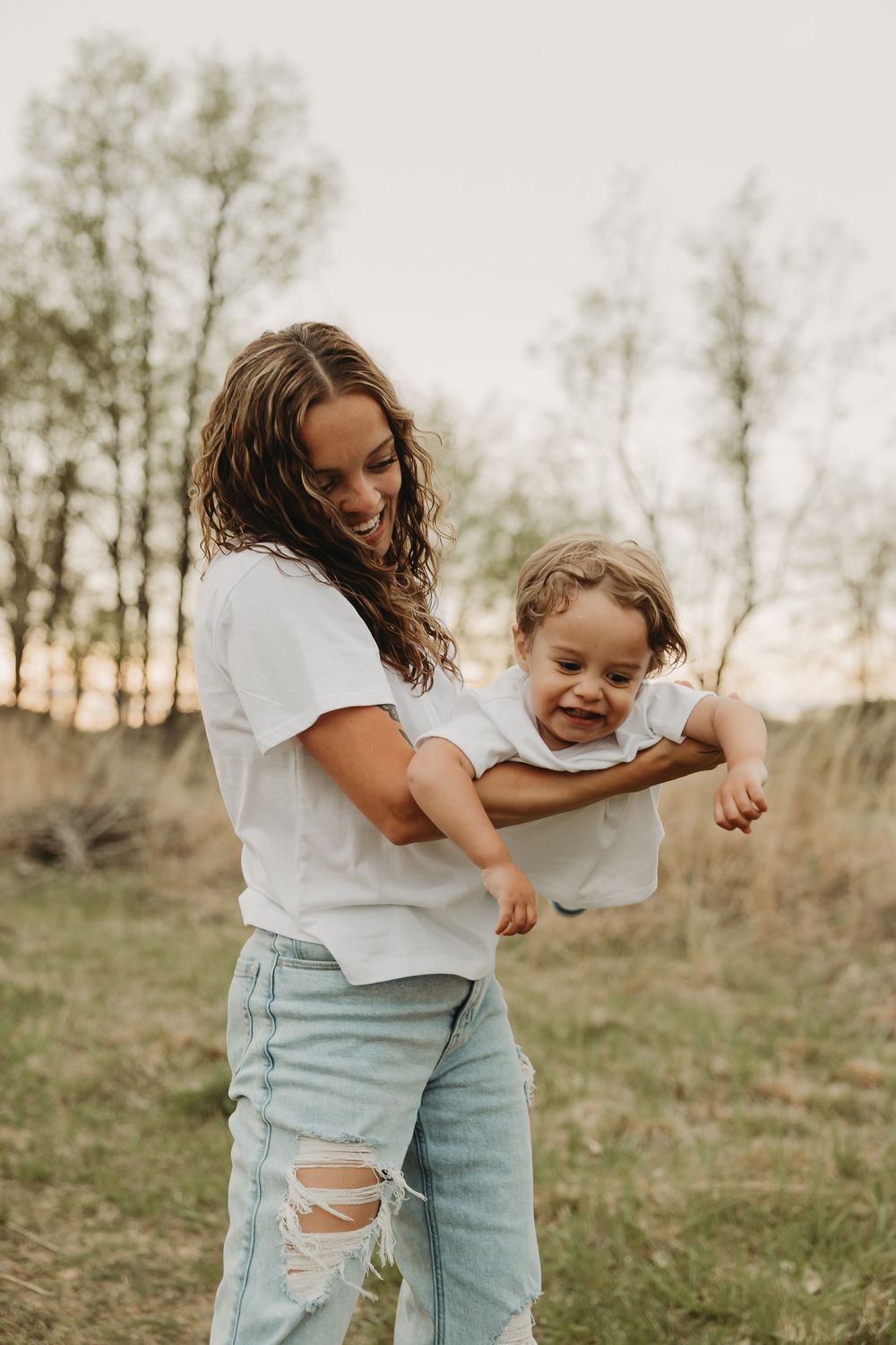 A parent and child share a playful moment together outdoors at sunset in a grassy field.