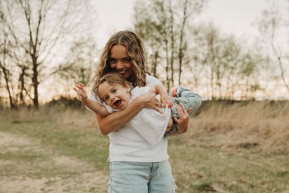 A candid outdoor moment between parent and child playing and laughing in a natural field setting at sunset.