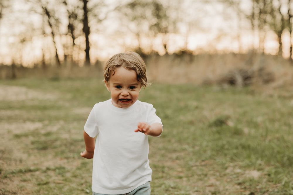 A young child in a white t-shirt runs and laughs joyfully in a grassy field at sunset.