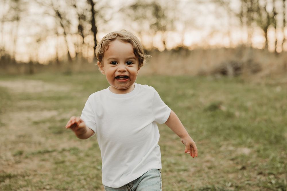 A candid moment captures a laughing child in a white shirt running through an open field.