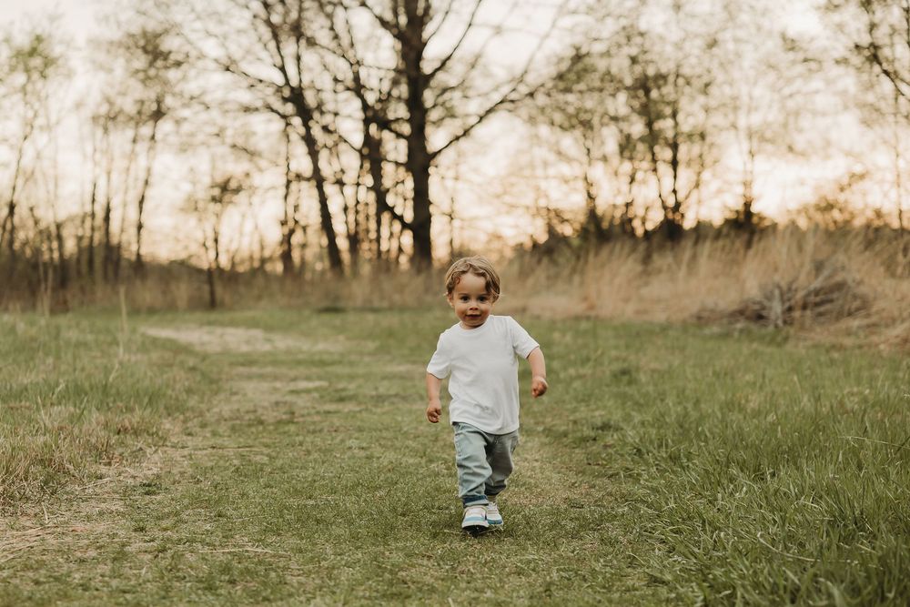 A small child running through a grassy field at sunset wearing a white t-shirt.
