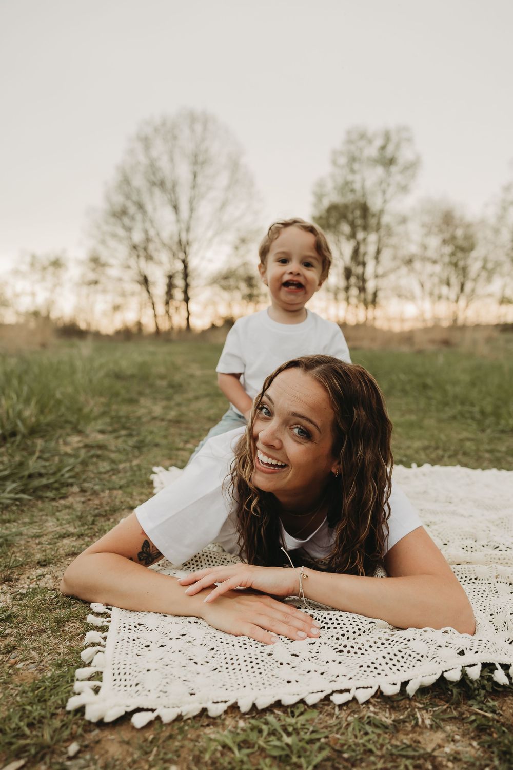 A joyful outdoor photoshoot on a white crochet blanket in a grassy field at sunset.