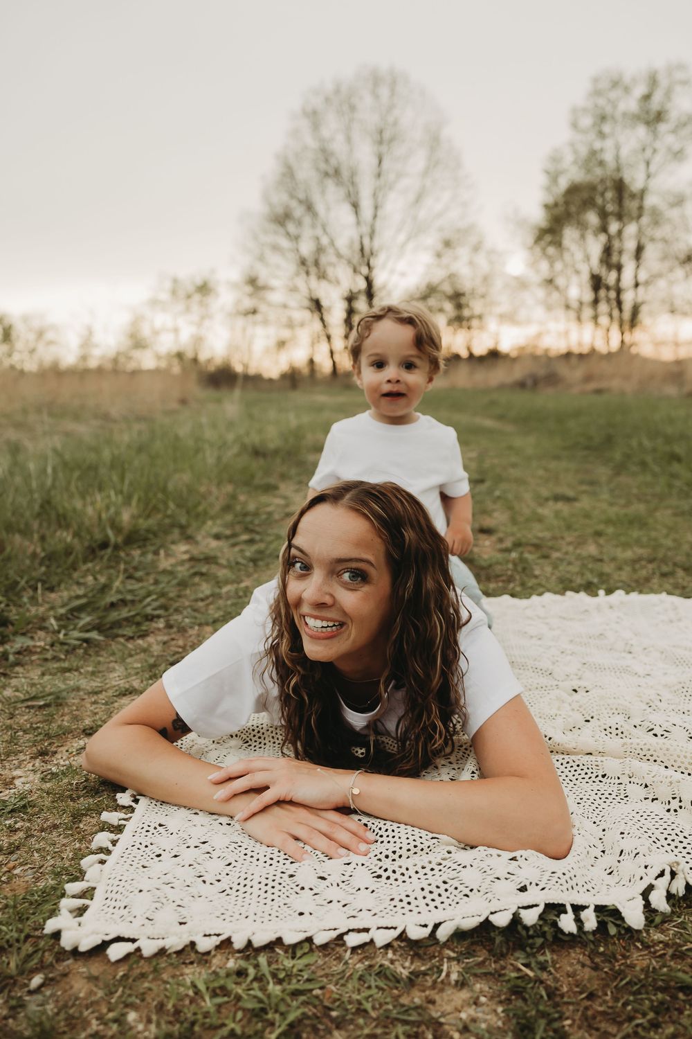 An intimate outdoor portrait session on a decorative white blanket with trees in the background.