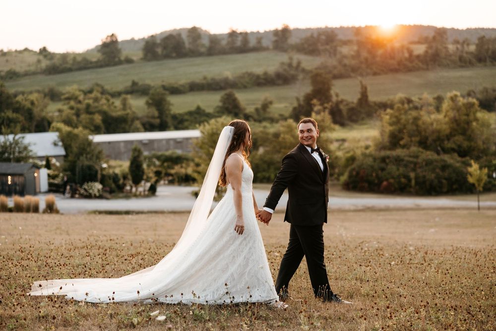 Romantic couple walks through golden fields at sunset during their wedding photoshoot in countryside setting.