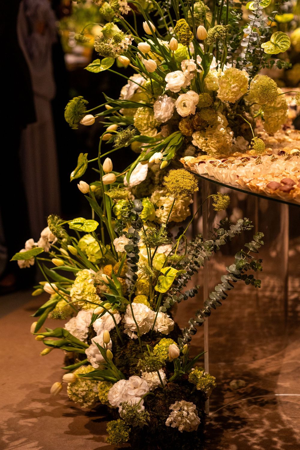 Elegant wedding floral arrangements in cream and yellow tones with lush greenery on wooden tables.