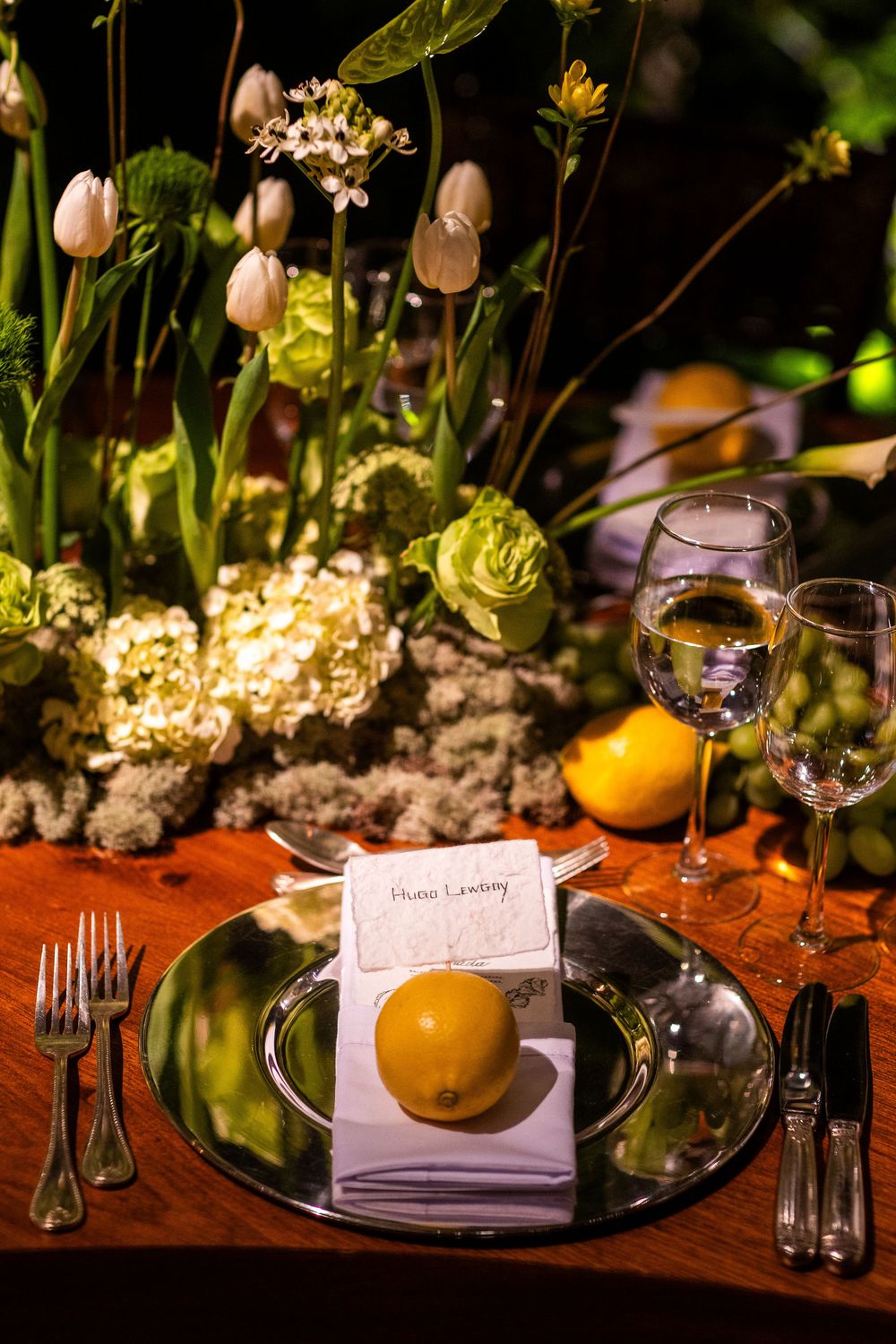Place settings with yellow citrus fruits and delicate tulips on dark wooden tables for an elegant reception.