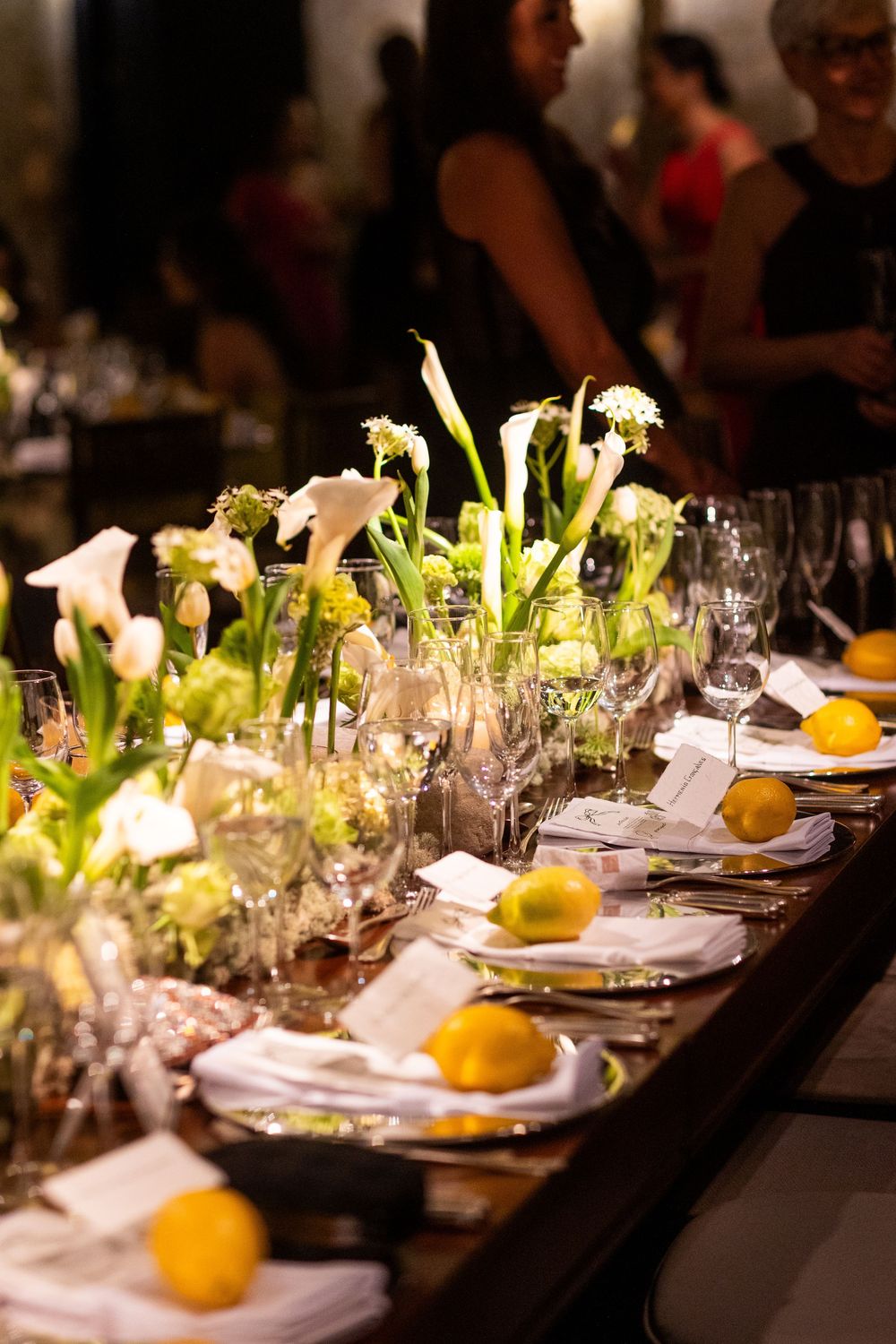 Formal dining table with place settings adorned with fresh celery stalks and oranges in an elegant dark setting.