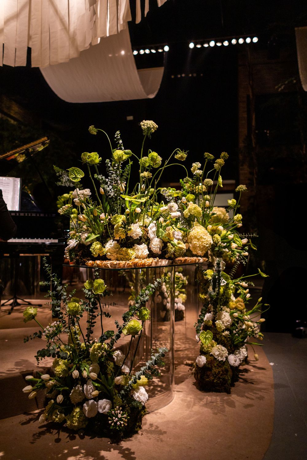 Elegant floral arrangement with green and white blooms on a stand against a dark background with stage lighting.