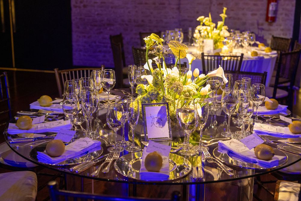 An elegant wedding table setting with crystal glassware and illuminated yellow floral centerpiece under purple lighting.