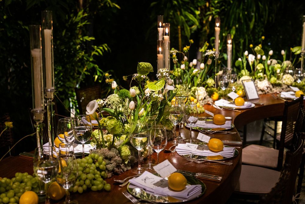 Elegant outdoor dining setup with rustic wooden tables and verdant greenery under string lights in a garden setting.