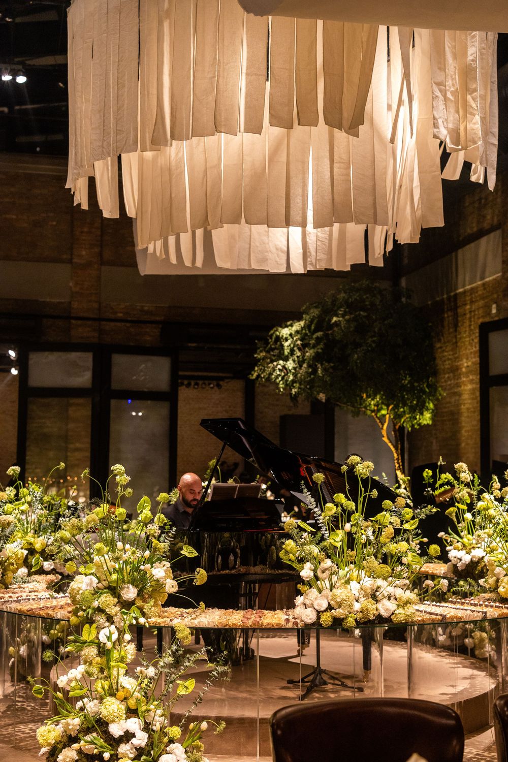 Modern indoor event space with white fabric ceiling drapes, floral arrangements and round dining tables.