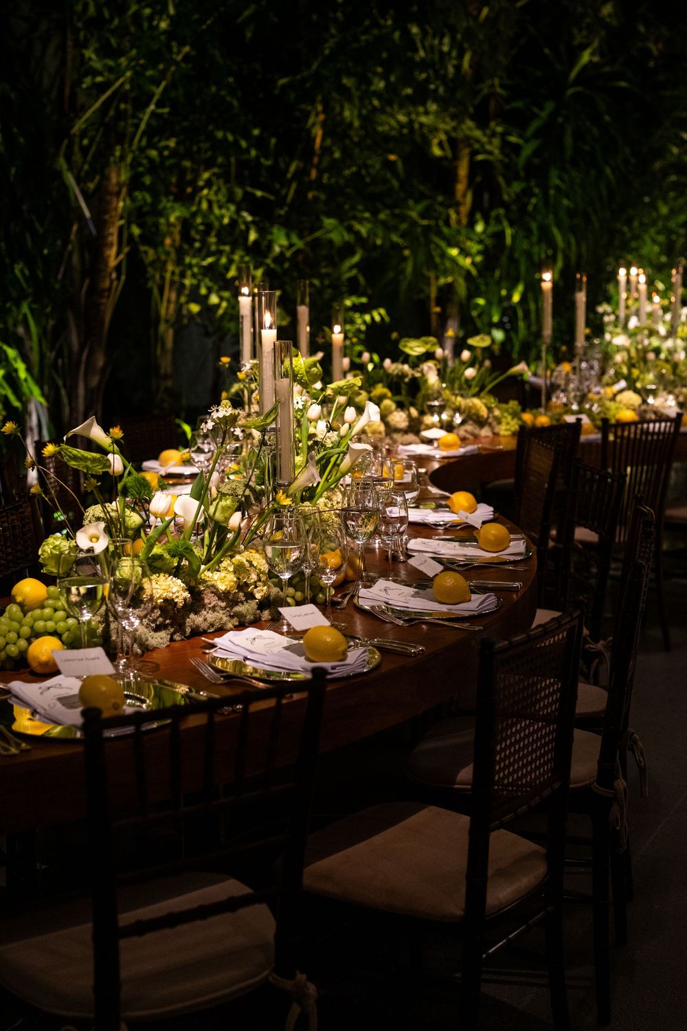 Dark elegant dining tables set with yellow citrus centerpieces and glowing candlelight create an intimate outdoor ambiance.