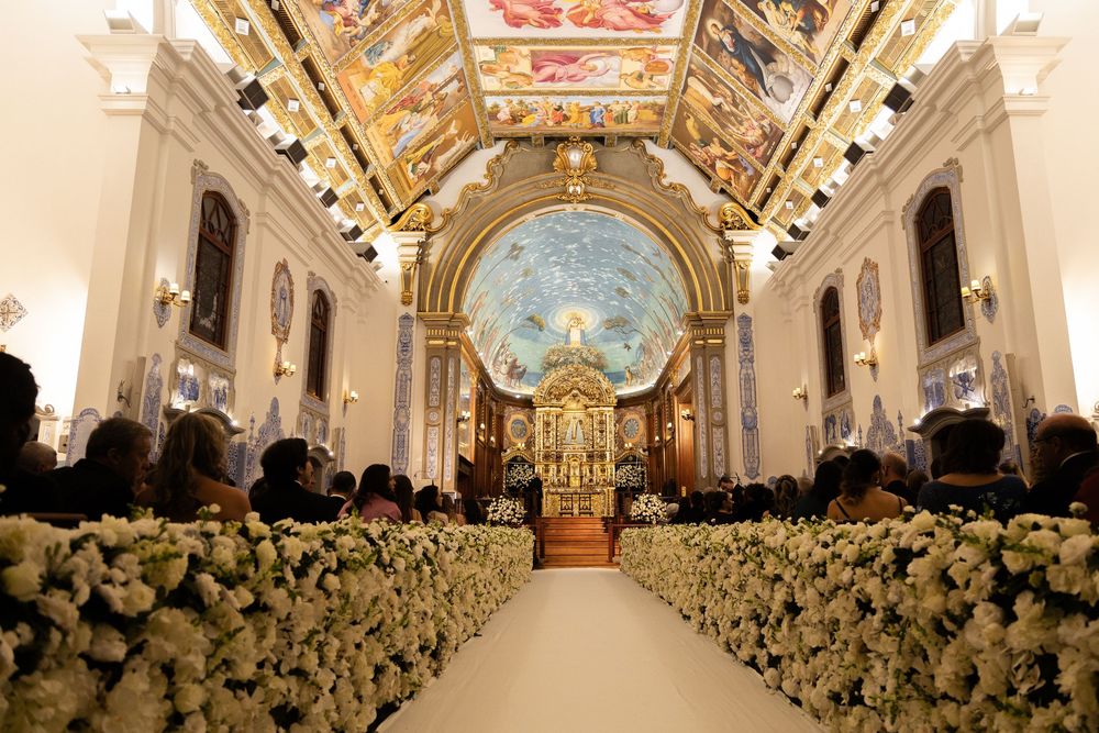 Ornate white cathedral interior decorated with luxurious floral arrangements lining the aisle for an elegant wedding ceremony.
