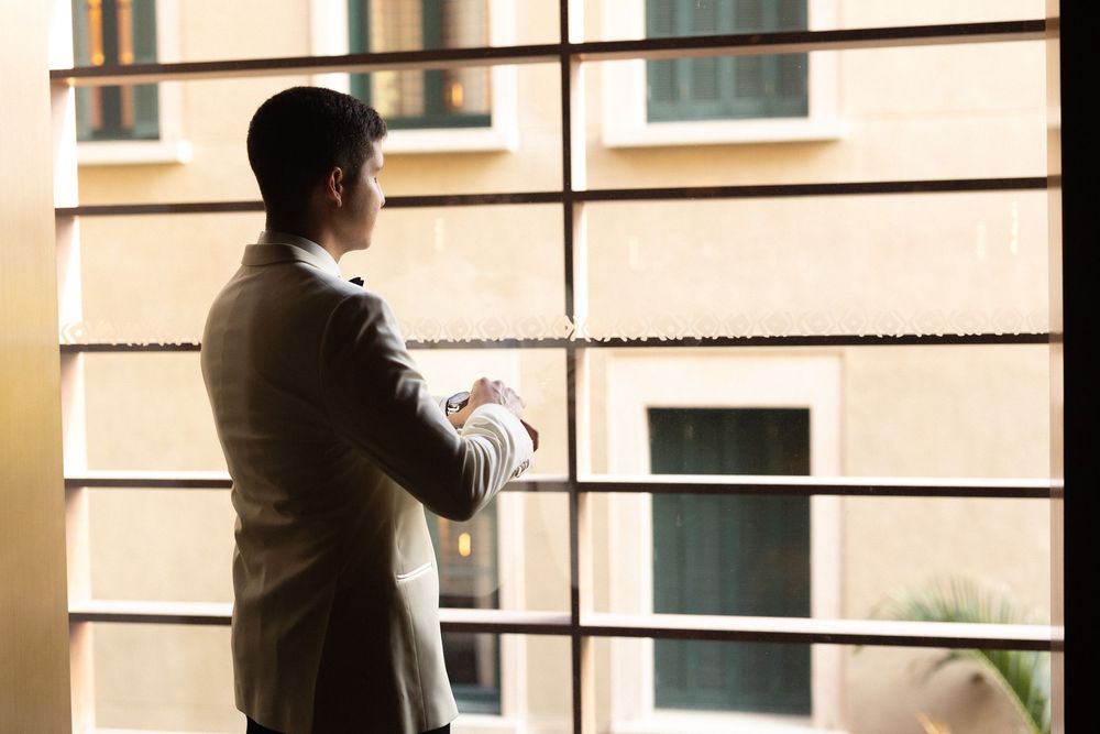 A silhouetted figure is seen through window blinds casting dramatic shadows in warm lighting.