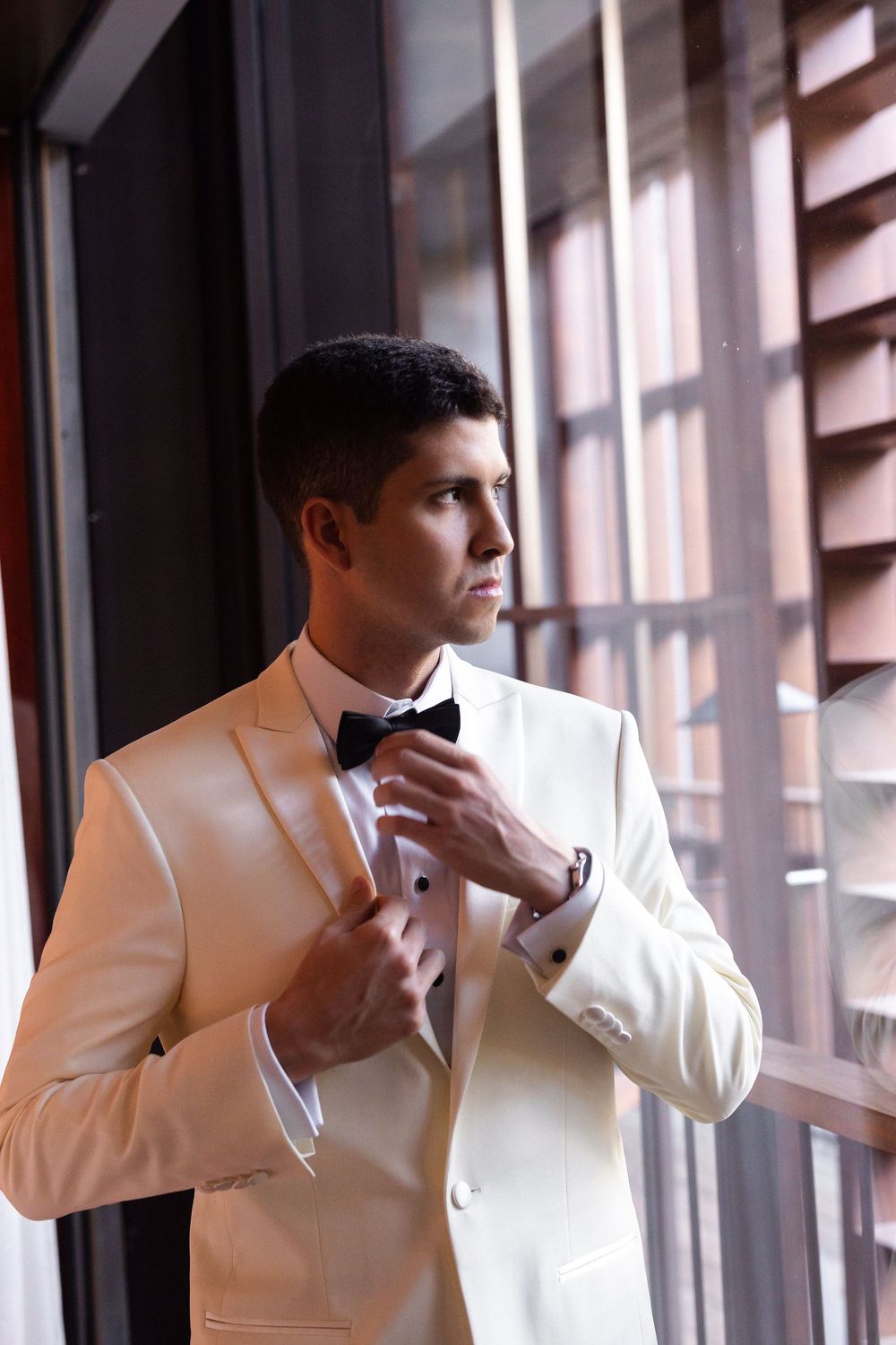 A person adjusts their bow tie near a window in a white tuxedo jacket, shown in multiple poses.