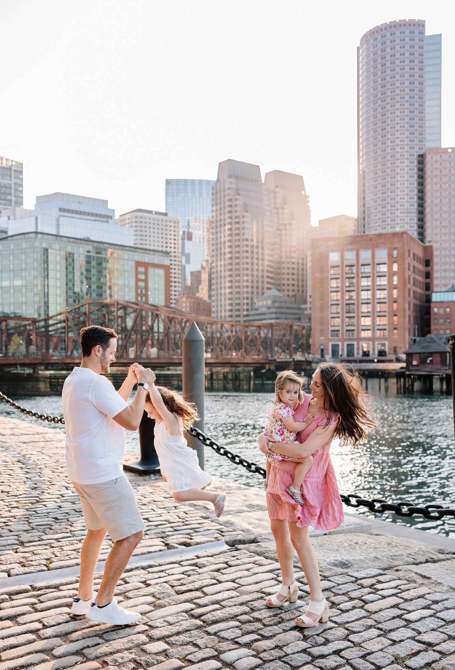 Series of playful photos showing friends dancing and having fun on cobblestone waterfront at sunset with city skyline behind.