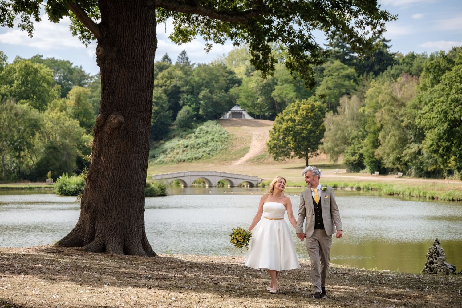 Scenic wedding photoshoot sequence in a lush park setting with stone bridge and lake views in the background.