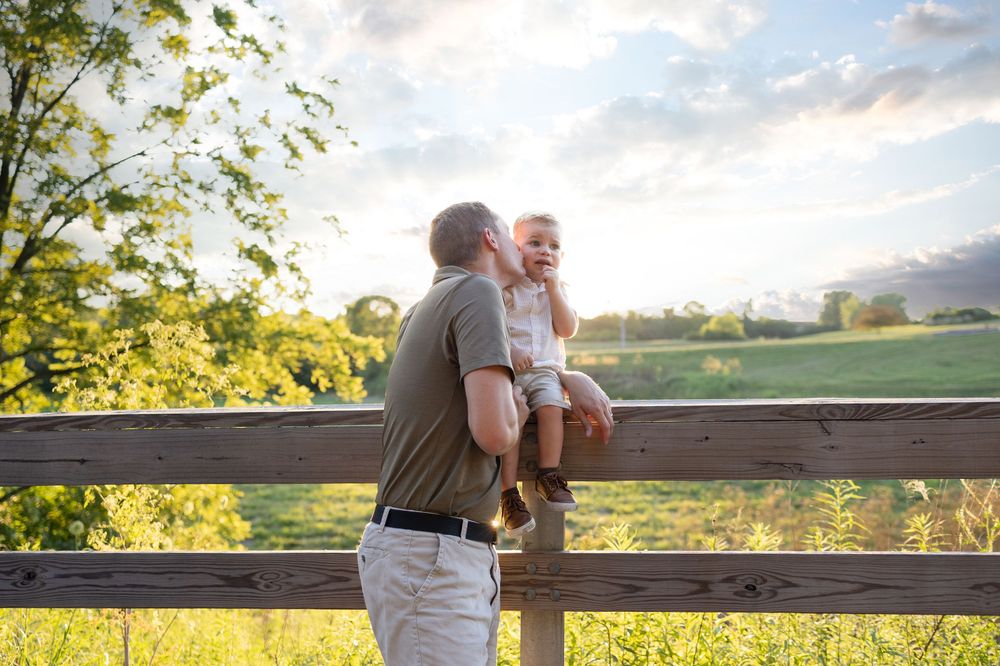 Springfield, IL Photographer captures a dad kissing his son's cheek on a fence in the country during a session in Central IL