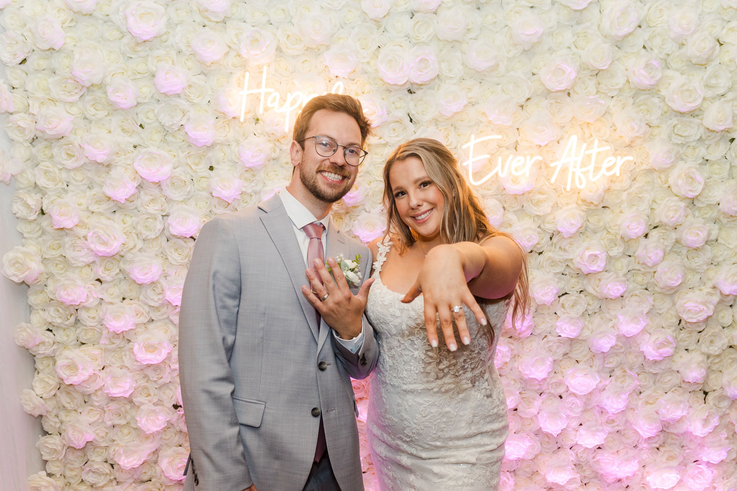 A happy couple celebrates their wedding day in front of a beautiful white and pink floral wall backdrop.