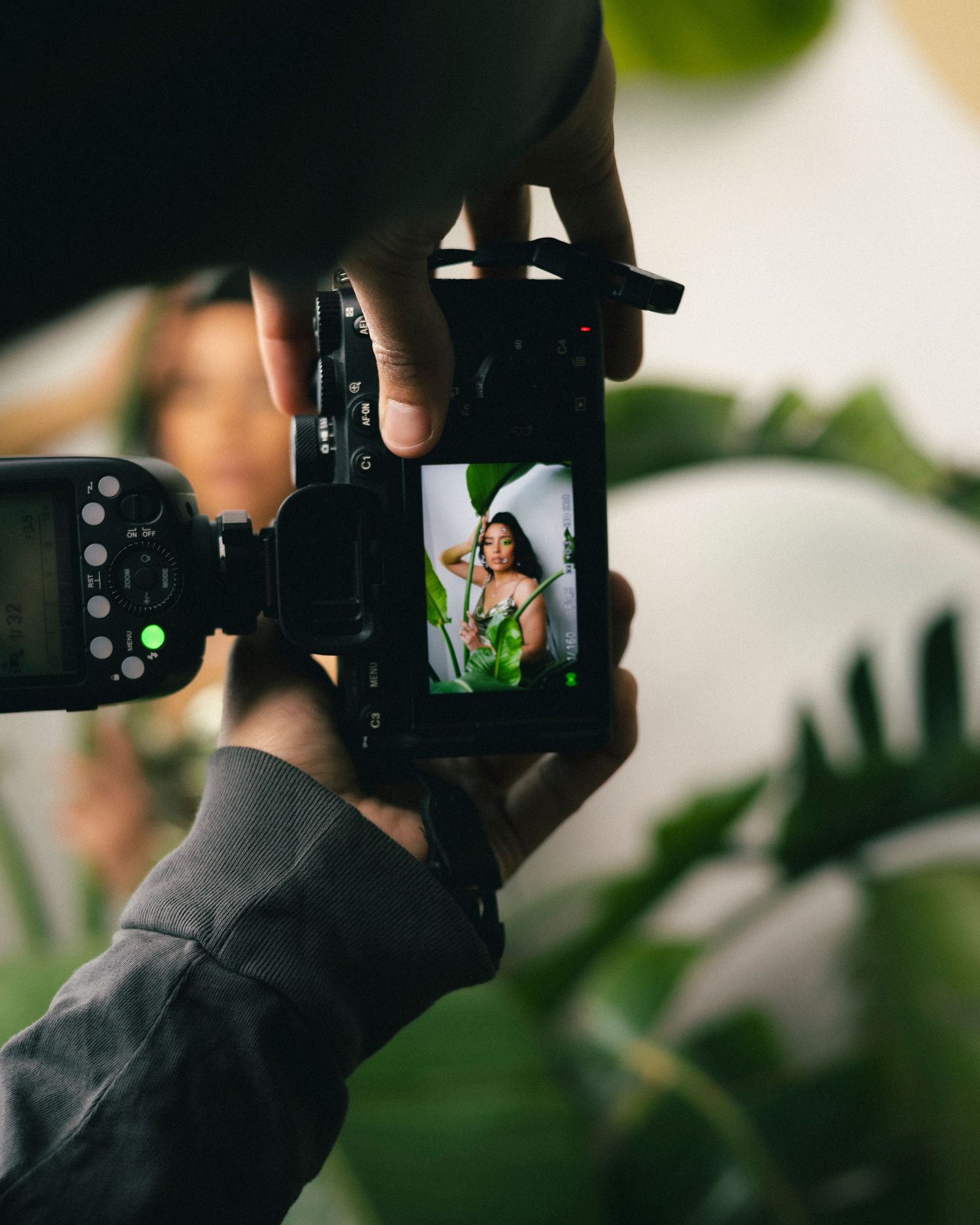 Photographer holds and operates a black digital camera with green foliage visible in the background.