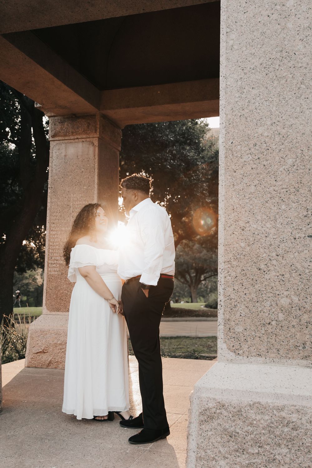 A romantic wedding couple shares tender moments under stone archways at sunset.