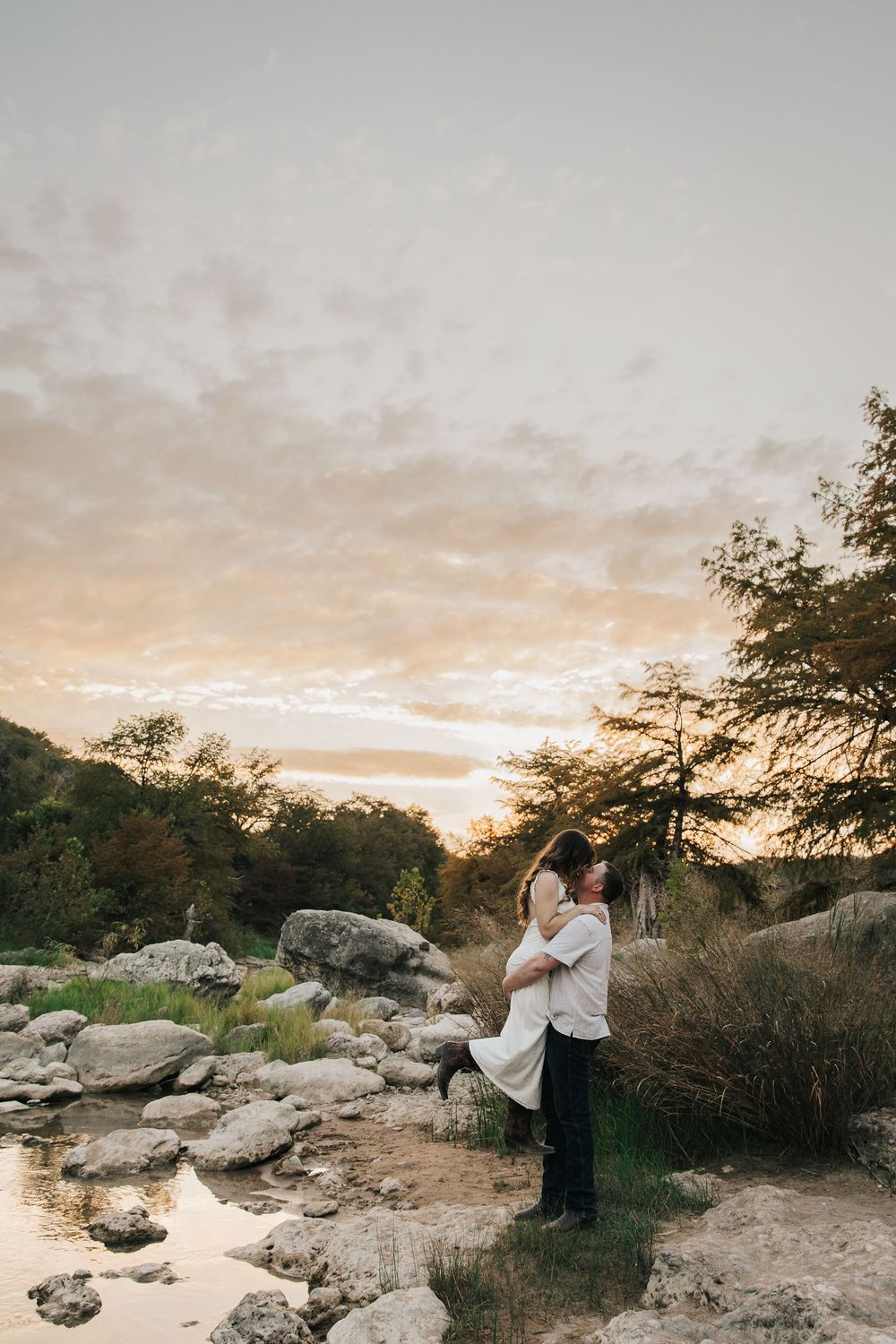 Couple in white and black attire poses together during sunset at a rocky desert landscape.