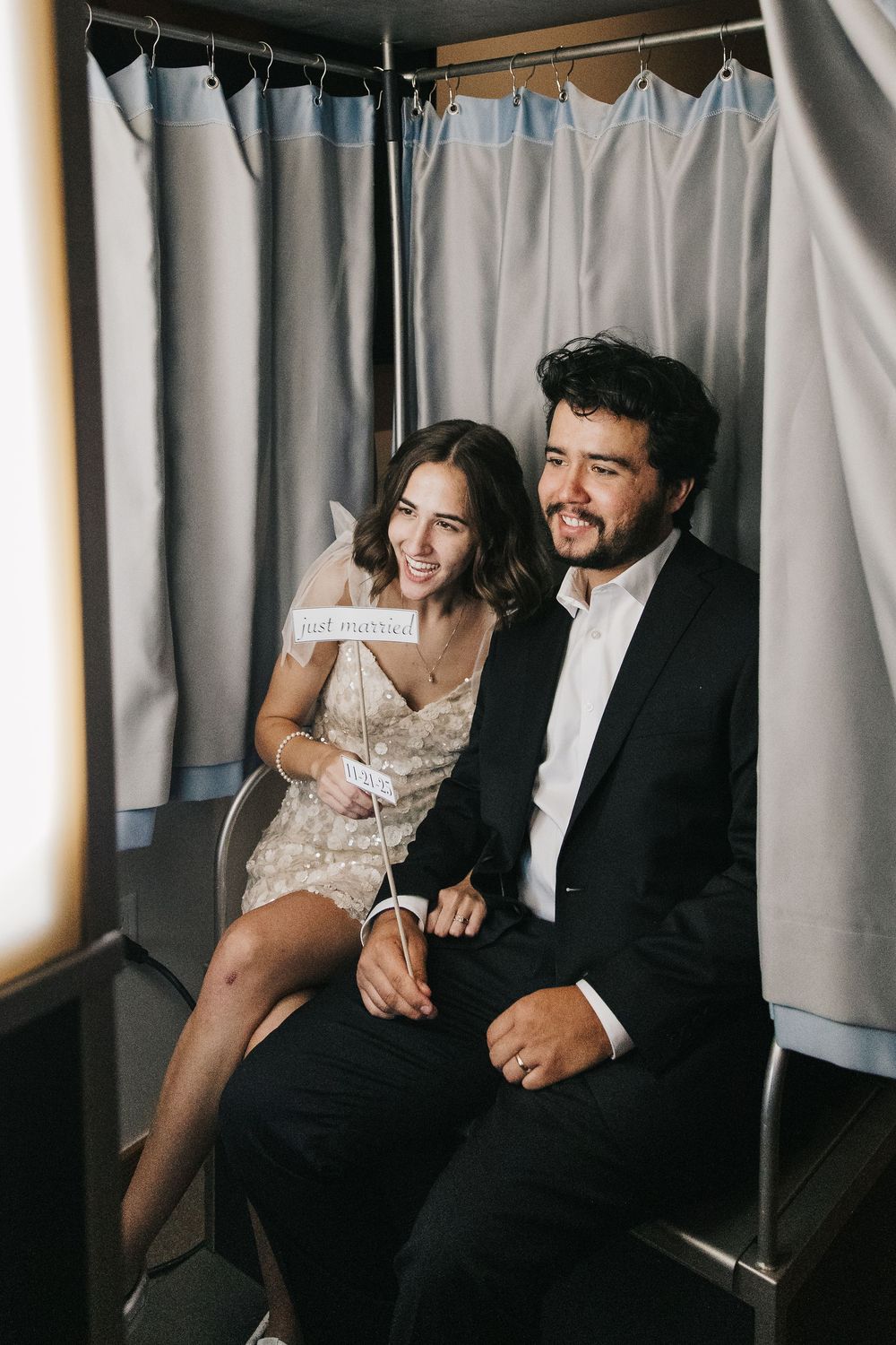 Couple sharing a candid moment while sitting together in a photo booth with grey curtain backdrop.