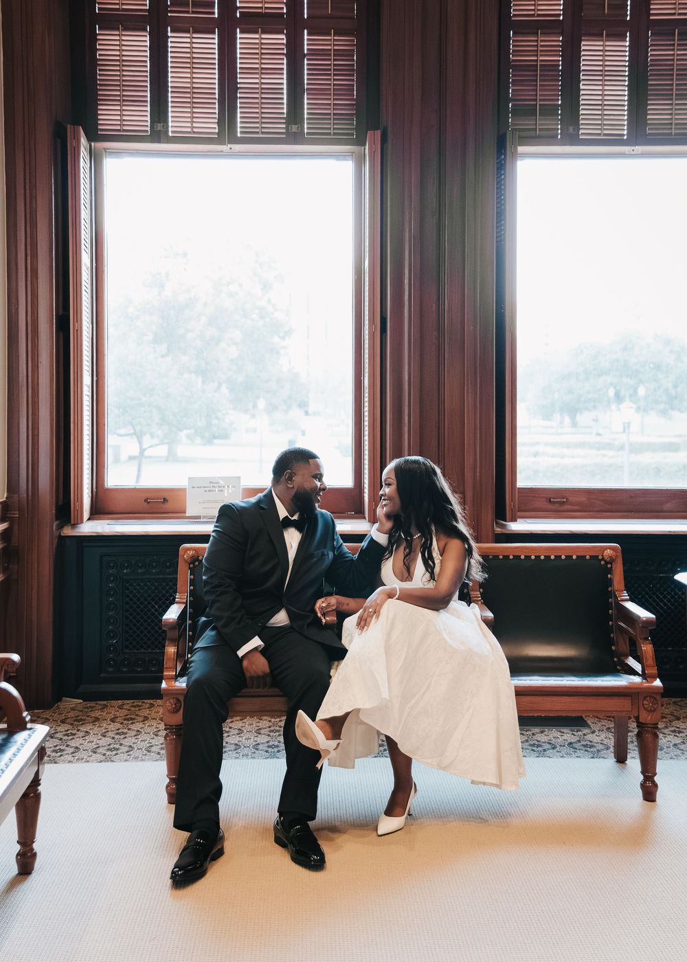 A couple in formal wedding attire sits together on a window bench in a sequence of playful poses.