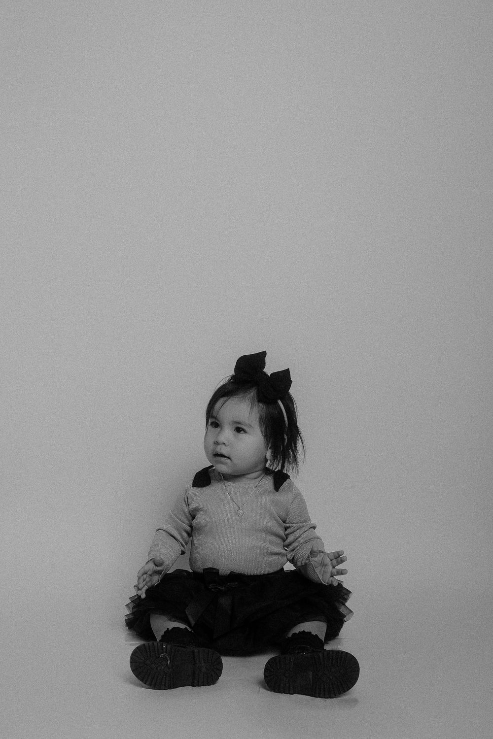 Black and white studio portrait of toddler against plain background.