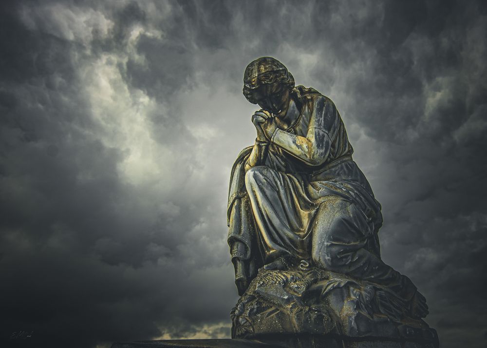 Ancient stone statues stand against a dramatic stormy sky with dark clouds swirling overhead.