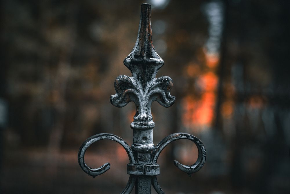Ornate cast iron metal detail of vintage lamp post against blurred dark background with orange glow.