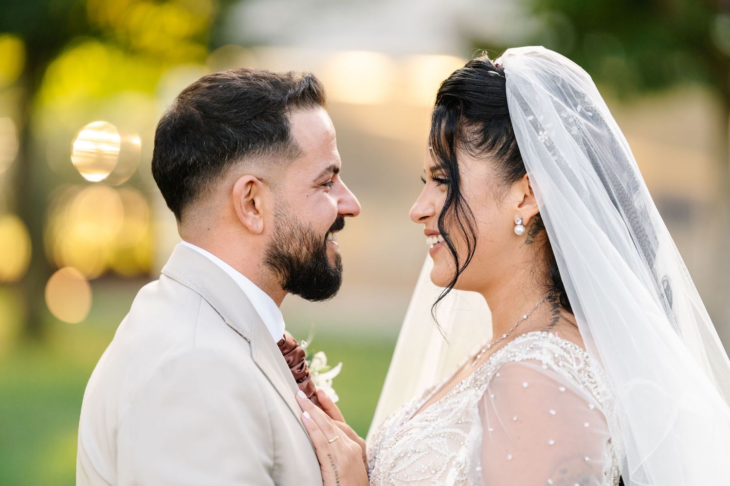 A joyful wedding portrait of a couple outdoors with sunlit trees in the background and a bridal bouquet with eucalyptus.