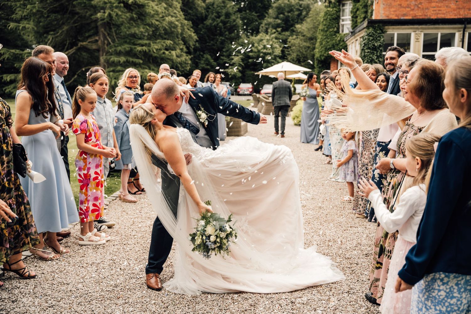 Wedding guests toss confetti over the newlyweds on a gravel path during outdoor celebration.