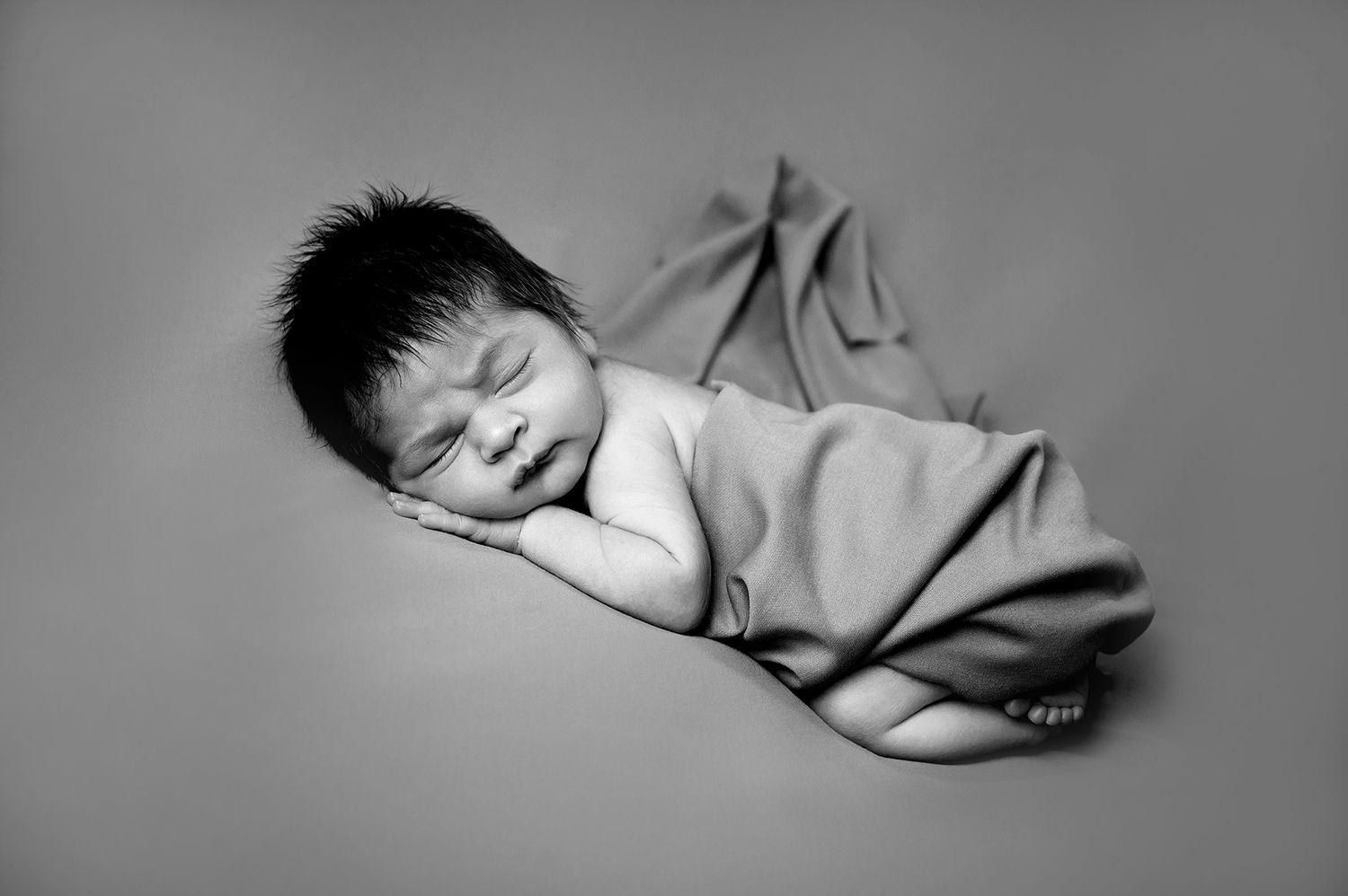 Peaceful sleeping newborn wrapped in soft gray blanket on neutral background.