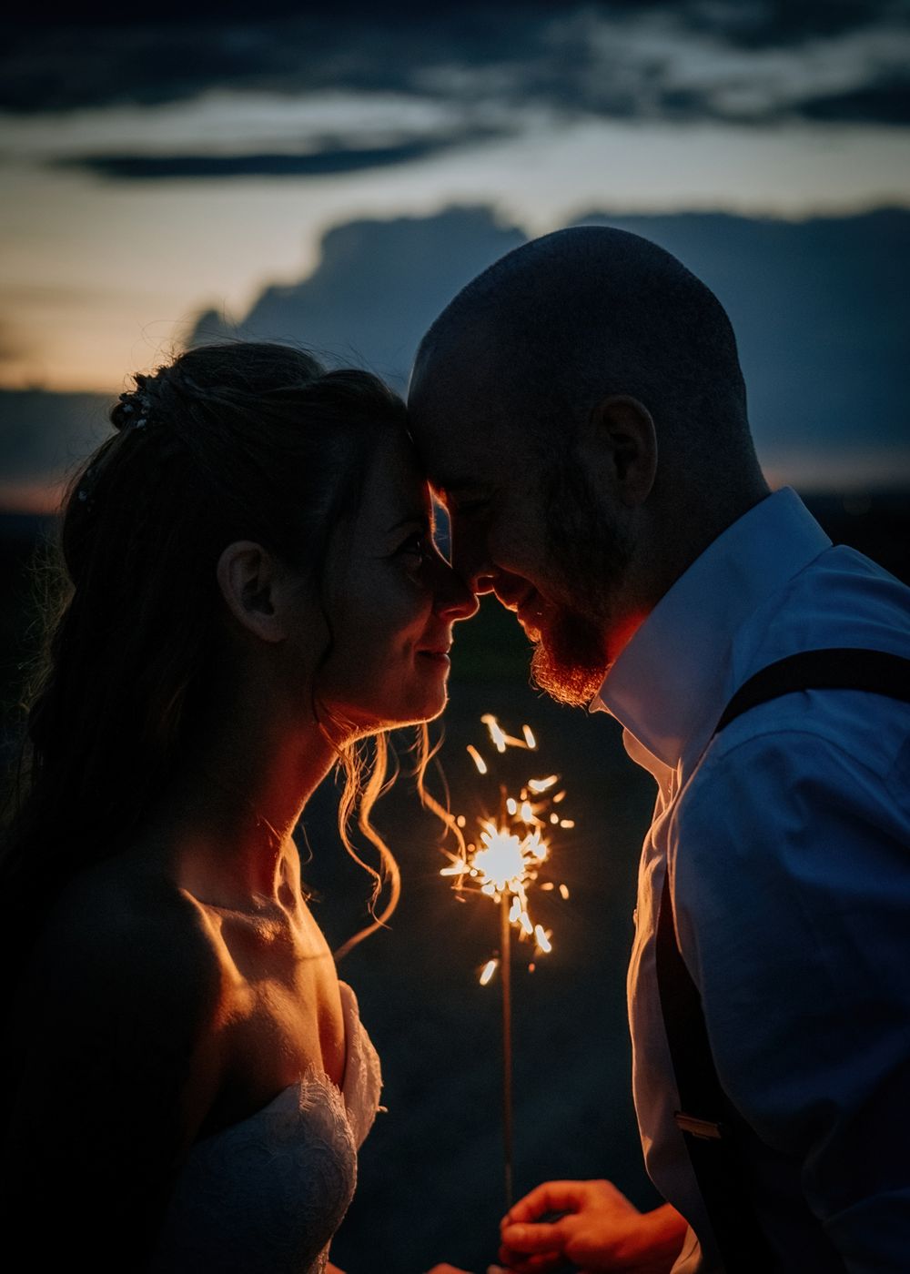 Couple's silhouettes illuminated by sparkler light against dusky mountain backdrop.