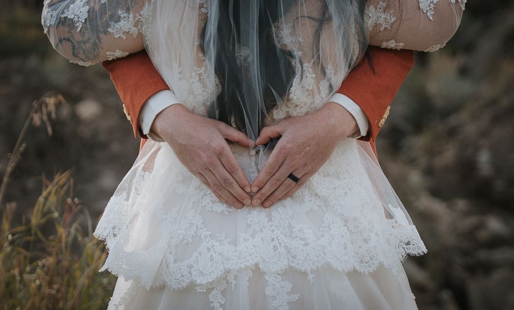 Close-up of hands forming a heart shape on a white lace wedding dress with orange sleeves.