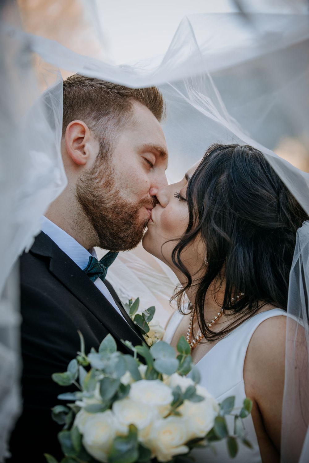 Romantic wedding portrait with white roses and flowing veil during an intimate moment.