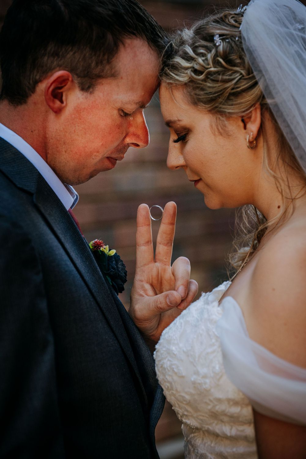 Intimate wedding portrait showing newlyweds touching foreheads while bride makes peace sign between them.