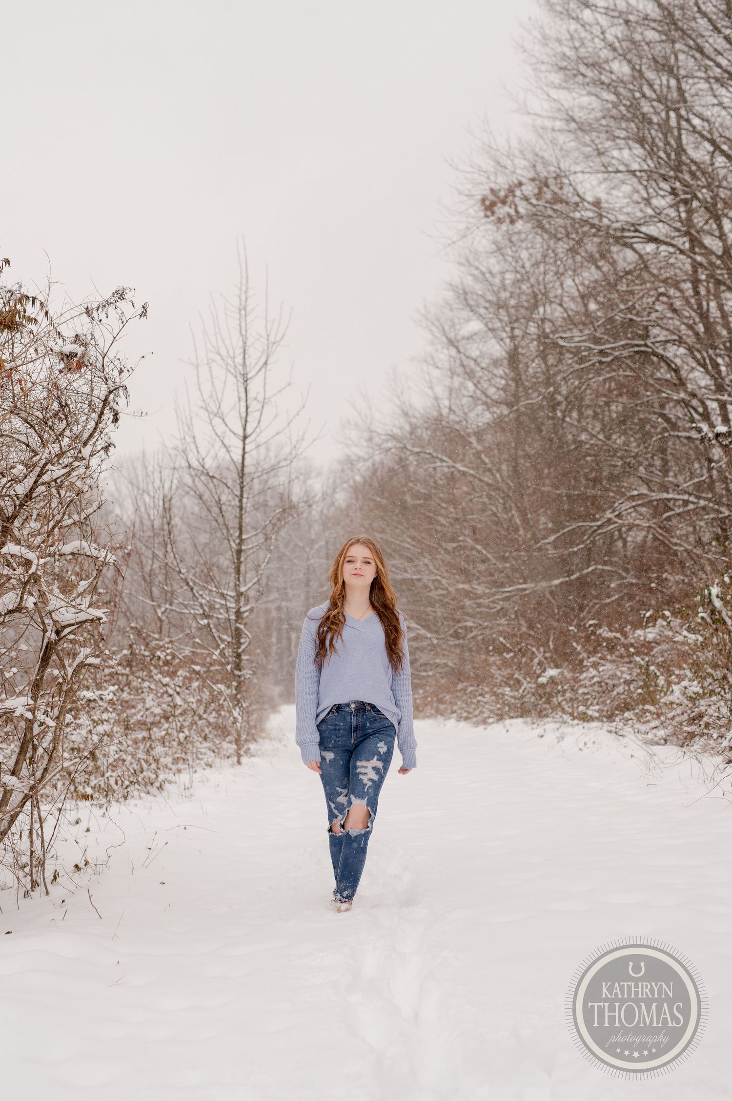Casual winter fashion photo on a snow-covered path with bare trees in the background.