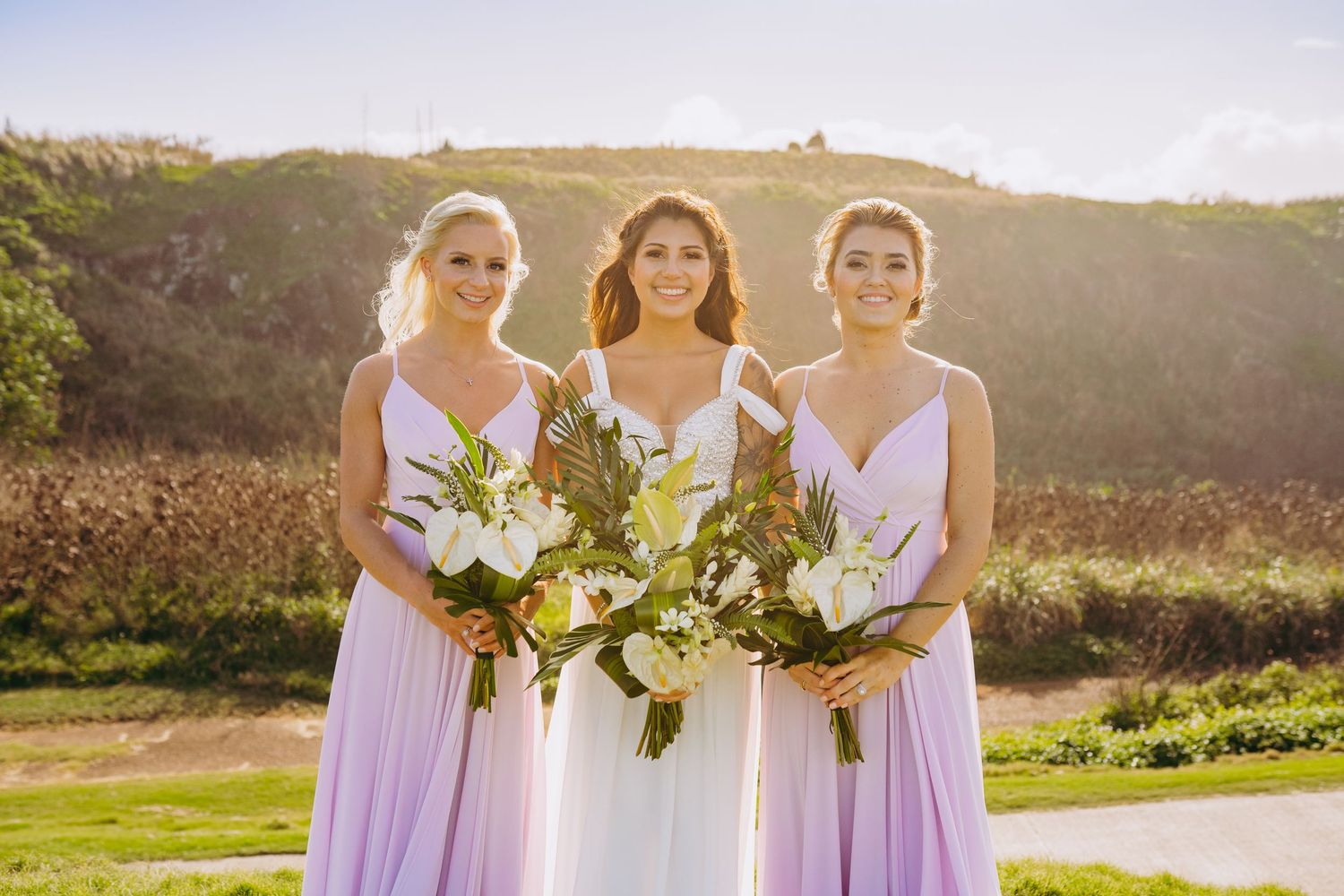 Bridesmaids in lavender dresses hold bouquets during sunset wedding ceremony. Maui Hawaii Oahu Kaneohe Bay wedding military wedding