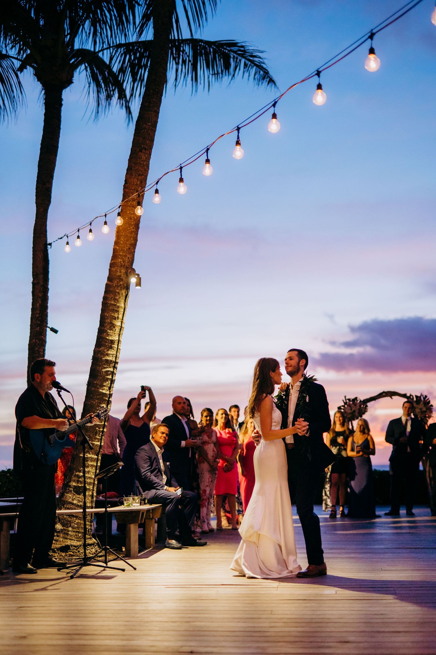 Evening wedding reception on an oceanfront deck with string lights and palm trees at sunset. Maui Hawaii Kaanapali Kapalua Merrimans wedding